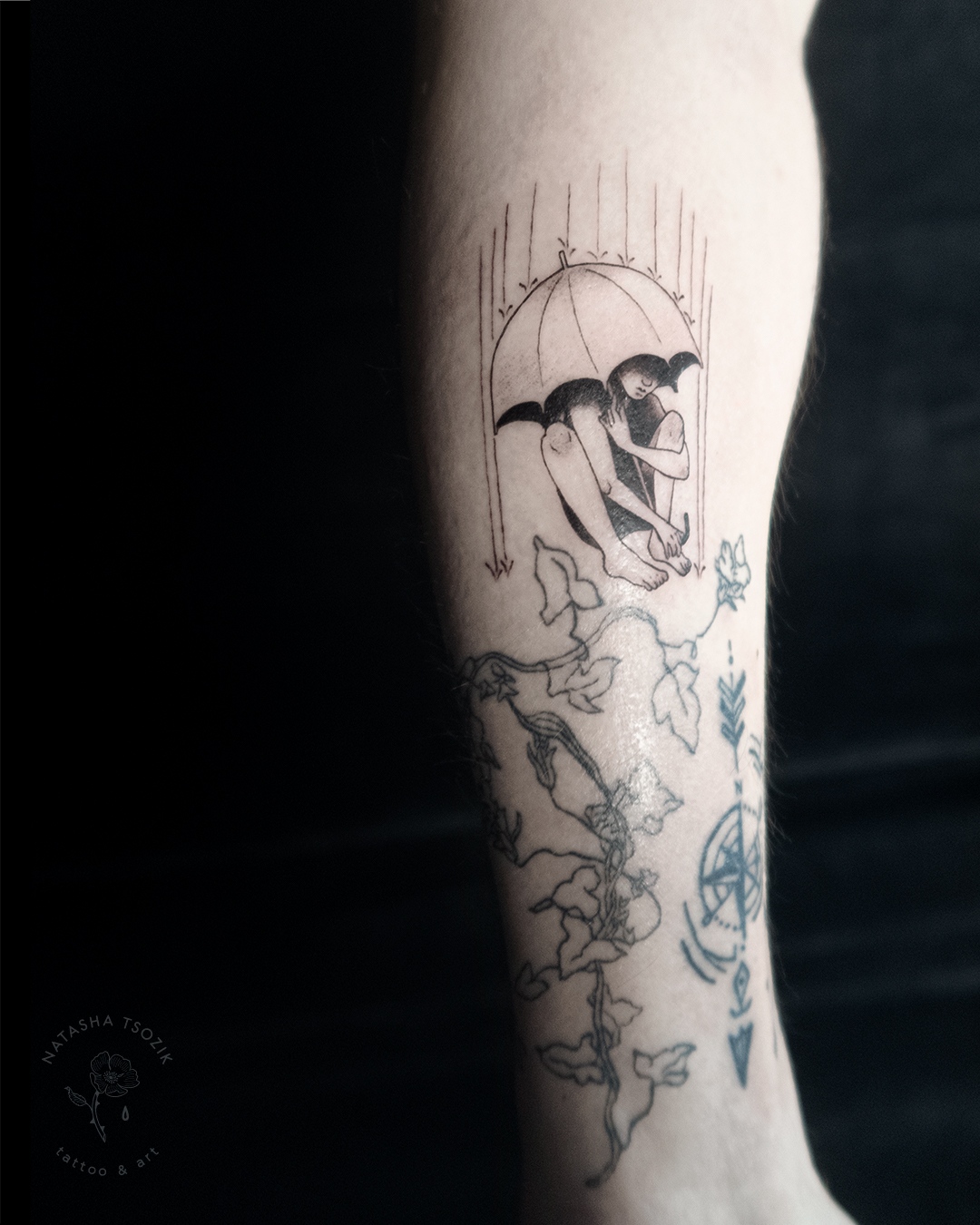 A forearm with small tattoos: Umbrella, Plant, Compass