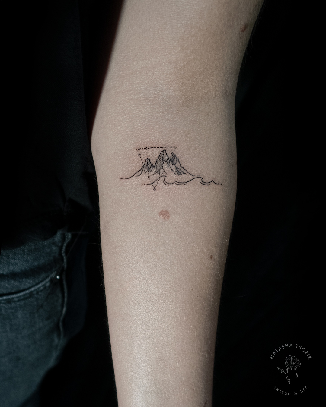 A small mountain and wave tattoo on a forearm