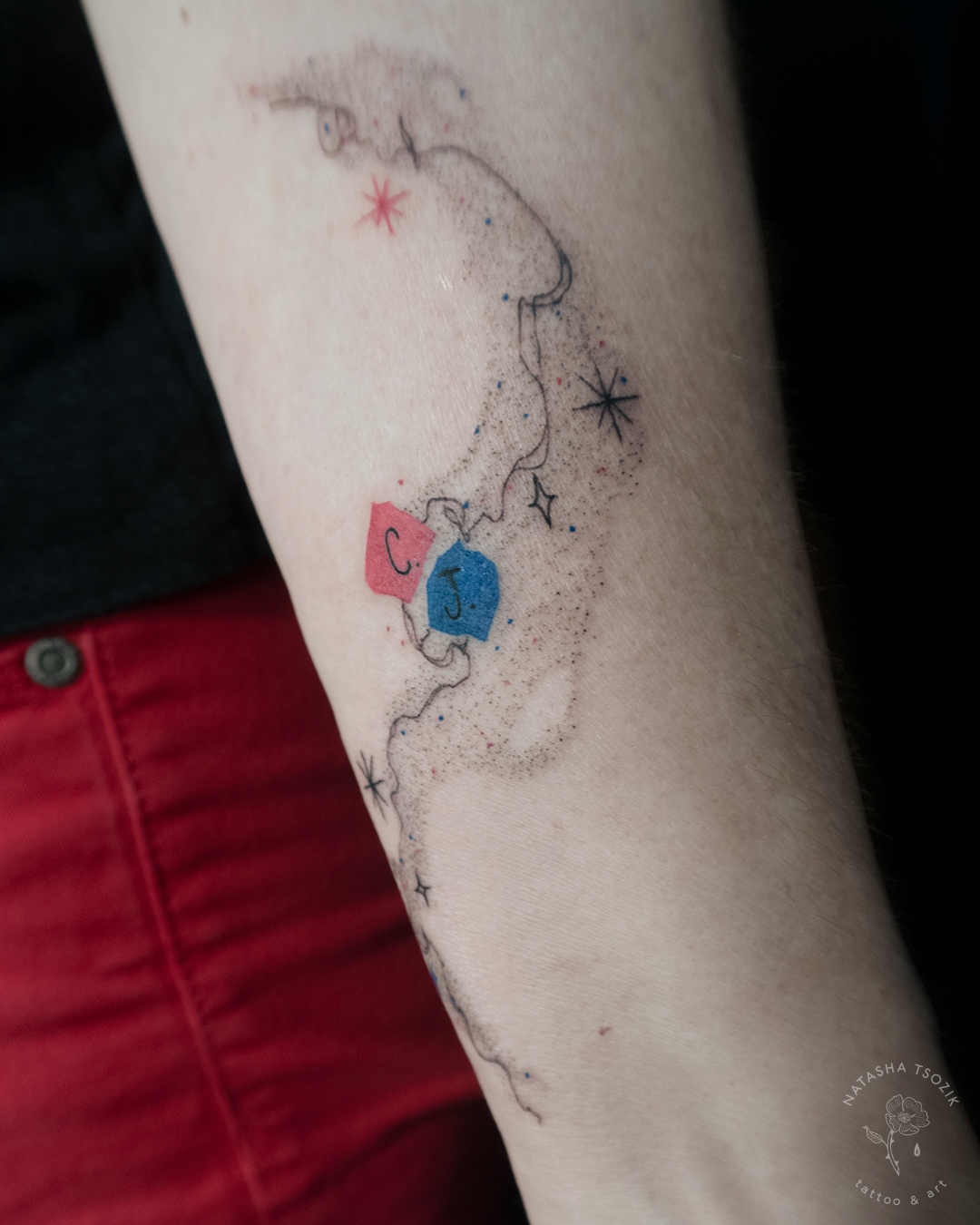 Star dust & initials tattoo on a forearm.