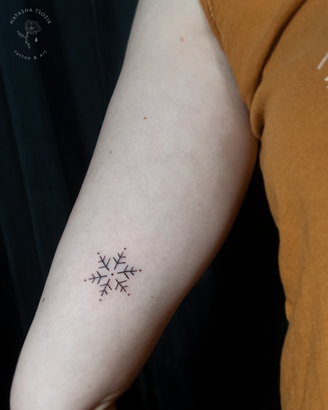 A minimalistic snowflake tattoo on an inner bicep.