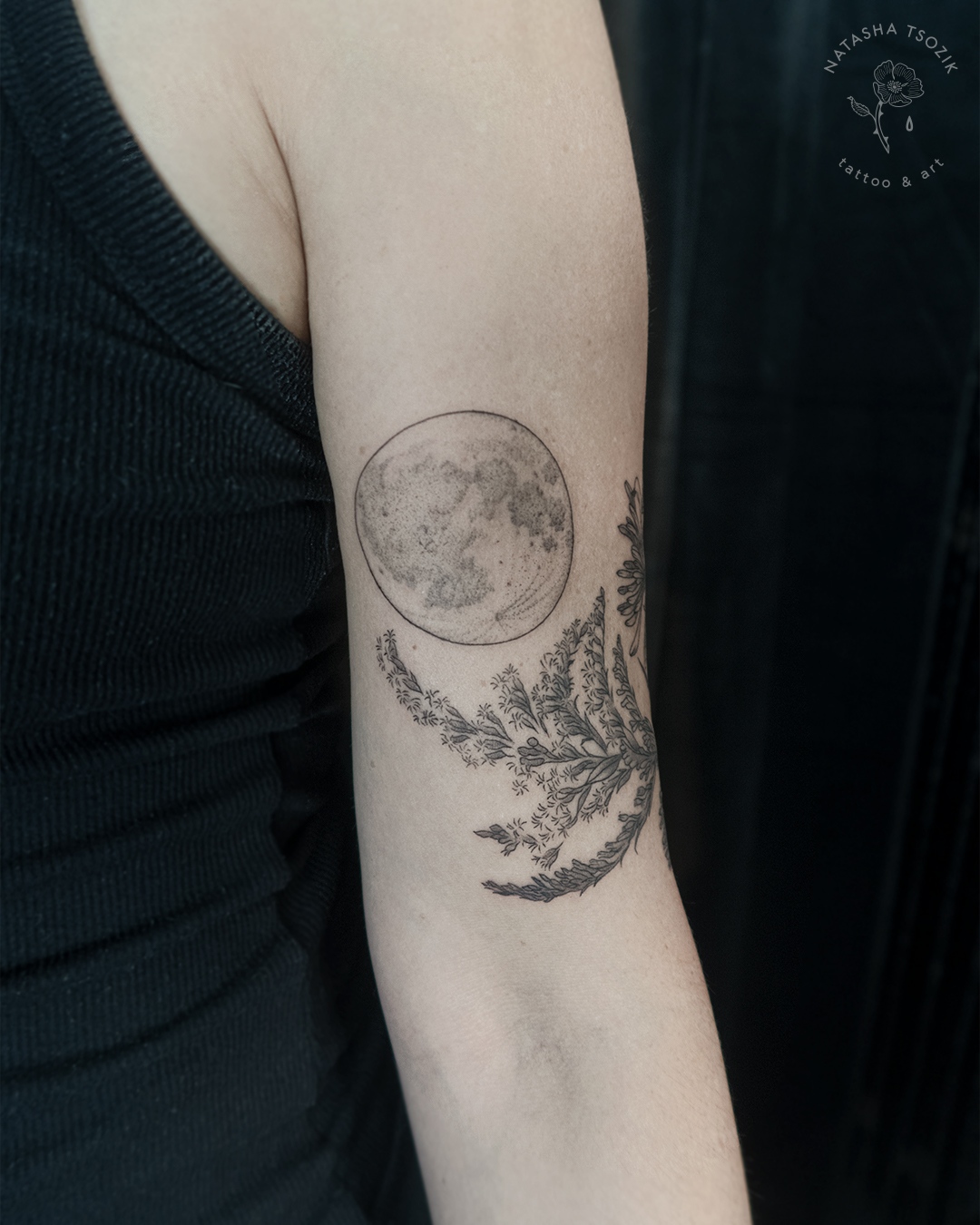 A close-up of a moon tattoo above a floral piece.