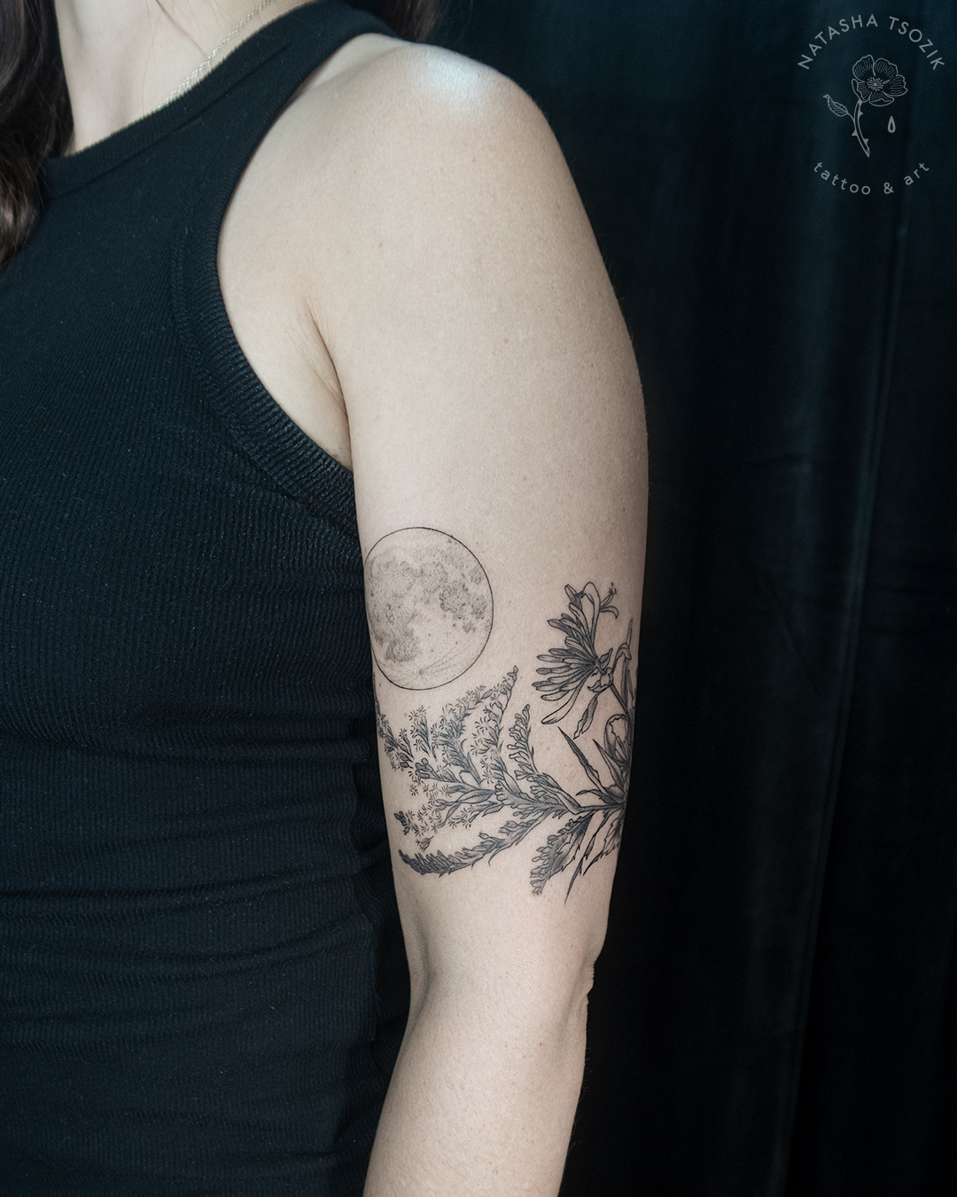 Botanical tattoo on a bicep: moon above a floral piece.