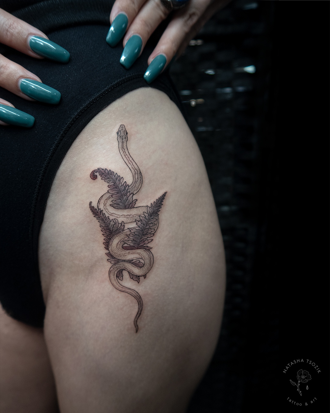 A snake with fern tattoo on a thigh.
